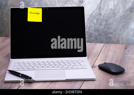 The photo shows a notebook on a wooden table, on the display is stuck the message knowledge Stock Photo