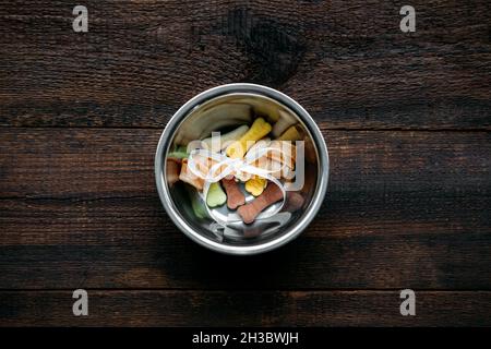 Dog bone in bowl on wooden background. Artificial bones and Mini Tiny Treats for pets. Long Lasting Dog Chew Bone and snacks Stock Photo