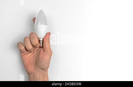 Hand with LED light bulb on a white table background with copy space Stock Photo