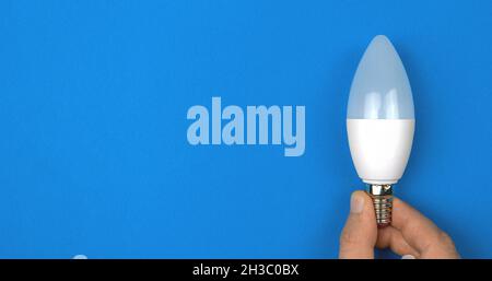 Modern eco LED light bulb in hand, blue background. Banner, flat lay, top view, copy space Stock Photo