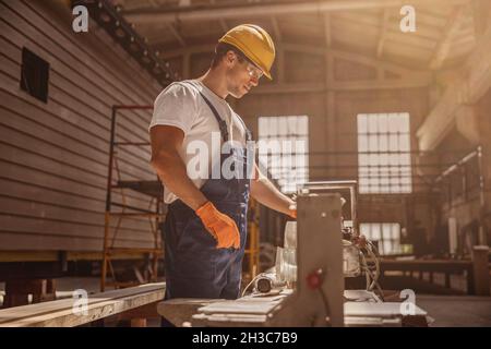 Handsome male builder using woodworking machine in workshop Stock Photo