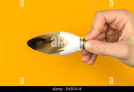 Hand with broken after fire LED light bulb. Concept of electrical short circuit. Burning wire in house, dangerous, failure. Home safety. Top view, ora Stock Photo