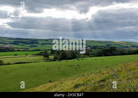 sun bursting through the clouds on the isle of purbeck in dorset uk. sun rays shining through grey autumn cloud and an overcast sky on isle of purbeck Stock Photo