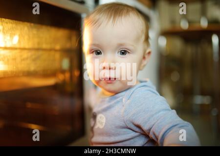 Little child playing with electric stove in the kitchen. Toddler boy near hot oven. Baby safety in kitchen. Stock Photo