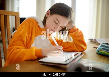 Preteen schoolgirl doing her homework with digital tablet at home. Child using gadgets to study. Education and distance learning for kids. Homeschooli Stock Photo