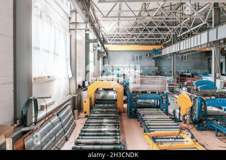 Industrial factory workshop or warehouse interior inside for metal roof tiles production. Production of roofing on automated conveyor belts and lines equipment. Stock Photo