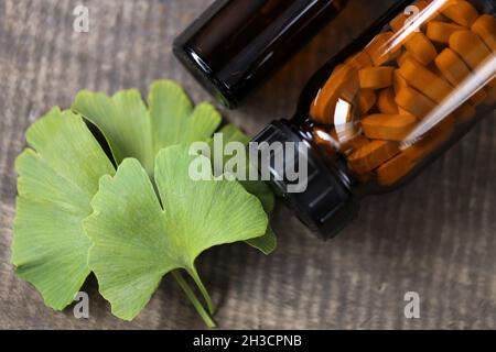 Ginkgo biloba pills .Brown glass jar with homeopathic pills with ginkgo extract and ginkgo leaves on wooden background .  Stock Photo