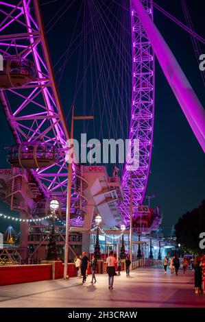 LONDON - SEPTEMBER 14, 2021: The lower half of The London Eye with people passing by at night. Colourfully illuminated. Stock Photo