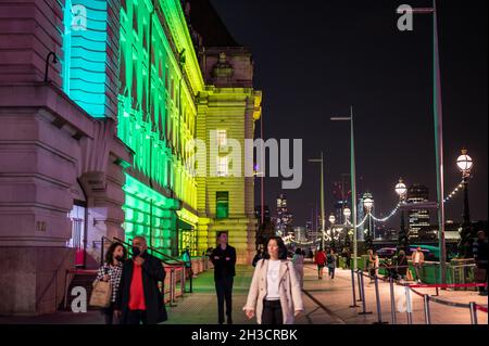 LONDON - SEPTEMBER 14, 2021: People walking at night next to colourfully illuminated County Hall at night. Stock Photo