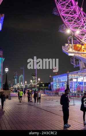LONDON - SEPTEMBER 14, 2021: Colourful night scene as people walk beneath the London Eye at night. Stock Photo