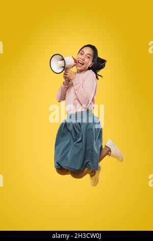 Cute girl jumping and screaming making announcement using megaphone Stock Photo