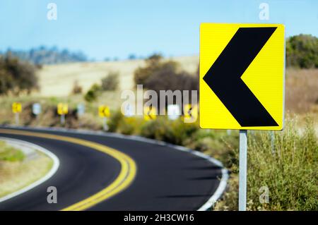 Curve signposted to the left on country road Stock Photo