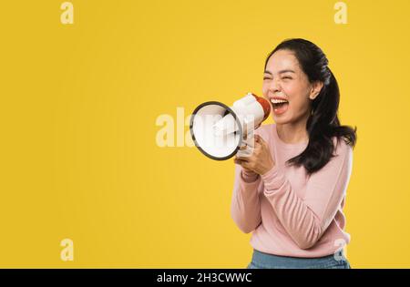 Asian woman screaming while holding megaphone with two hands making announcement Stock Photo