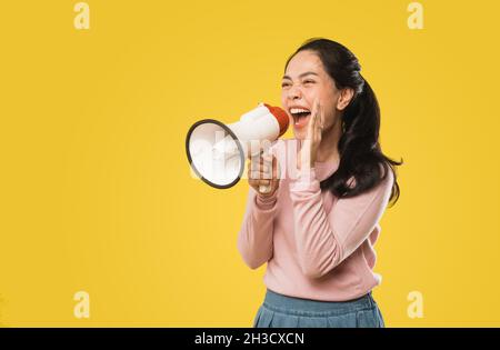 Asian woman screaming while holding megaphone with two hands making announcement Stock Photo