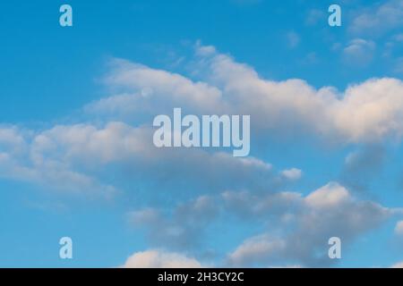 A calming peaceful image of puffy white clouds floating in front of the moon in the clear blue sky. Stock Photo
