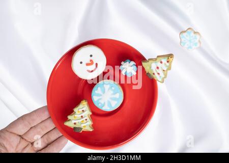 A hand touching a red plate with levitating Chriistmas theme cookies. Stock Photo