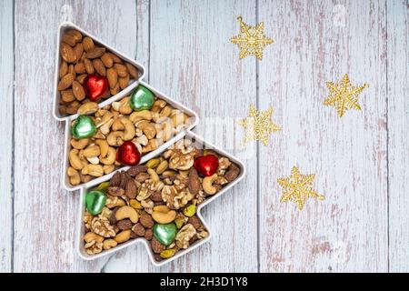 Mixed nuts and gold Christmas ornaments in a pine shape plate on light blue wooden background. Stock Photo