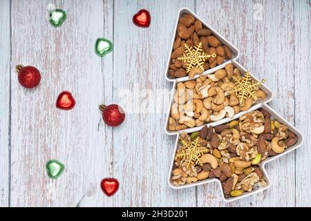Mixed nuts and gold Christmas ornaments in a pine shape plate on light blue wooden background. Stock Photo