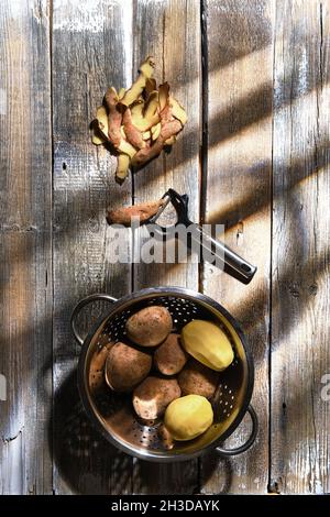 Top view of fresh potatoes and potato peelings with a knife on a table Stock Photo