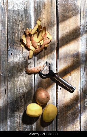 Overhead view of fresh potatoes and potato peelings with a knife on a table Stock Photo