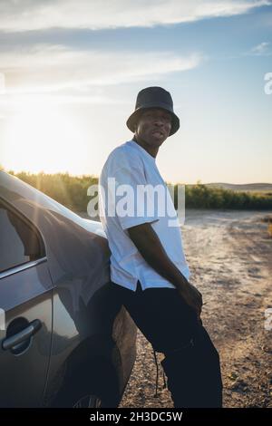 Portrait of a young black handsome man wearing a bucket hat posing outside by his car at sunset Stock Photo