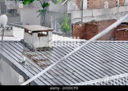 Rainy day and wet roof of house made of metal panels. Corrosion exists on roof and old style chimney stack during overcast weather. Stock Photo