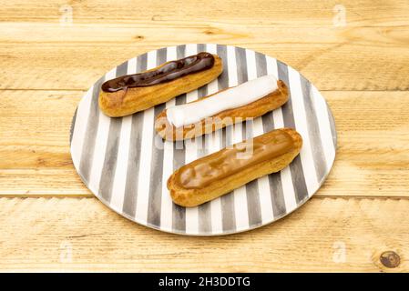 Tray of eclairs covered with three different chocolates on grated plate and unvarnished wooden table Stock Photo