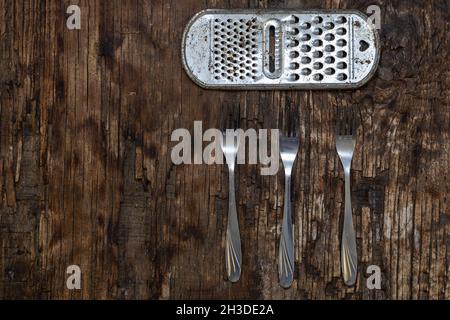 Old Metal kitchen utensils. Three stainless steel forks. Rusty kitchen grate against a rotting board. Wooden background. Top view. Selective focus. Stock Photo