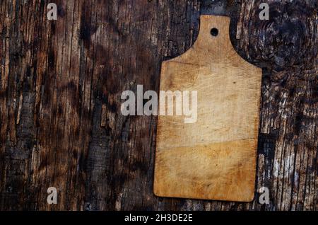 An old wooden cutting board on a black and brown wooden background. Texture of weathered burnt wood. Top view. Copy space Stock Photo
