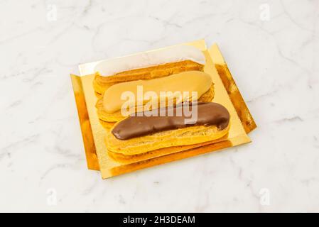 Tray of eclairs with topping of three different chocolates on white marble table Stock Photo