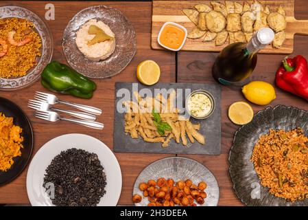 top view image of Spanish food tapas and dishes of black paella and Valenciana paella, with squid, fried eggplant, forks, patatas bravas and Russian s Stock Photo