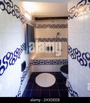 Front view bathroom with blue and white tiles. Down the hall is a bathtub with a shower. Nobody inside. Stock Photo