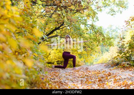 Sportive fit woman middle age exercise yoga fitness stretching in autumn fall forest with colorful foliage Stock Photo