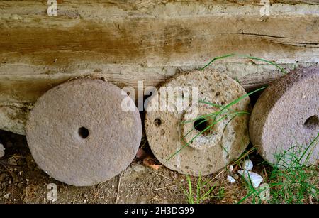 Round shape stone for wheat bran milling standing in village house in front of the wooden wallBricks wall made of mud in village house textured wall. Stock Photo