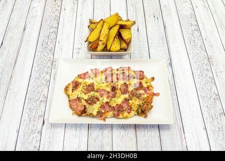 Veal schnitzel with lots of melted cheese and pieces of fried bacon and garnish of roasted potatoes cut into wedges Stock Photo