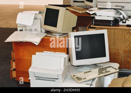 Old computers, printers, typewriters, keyboards ready to trash from office. Retro device, screens and monitors on table and floor Stock Photo