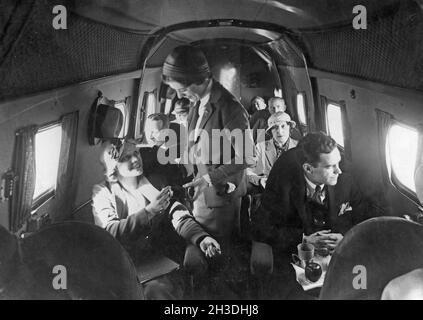 Airline travelling in the 1930s. A group of women and  men on an american passenger airplane in the 1930s. The female flight attendant is standing in the middle of the airplane servicing a young woman. Stock Photo