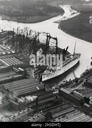 Dockyard in the 1930s. John Brown and company at Clydebank in Glasgow. The company built the famous cruise ships RMS Lusitania, HMS Hood, HMS Repulse, RMS Queen Mary, RMS Queen Elizabeth and Queen Elizabeth 2. Picture shows the ship The Empress of Britain and in the middle the first lower decks om the ship RMS Queen Mary being built. A work that started in december 1930. The ship was launched 1934. Picture taken 1931. Stock Photo