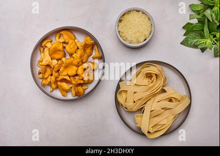 Ingredients for making italian pasta pappardelle with mushrooms chanterelles and cheese, on light table background, top view flat lay Stock Photo