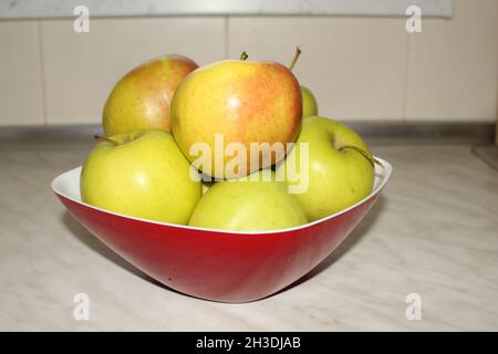 apples in a red bowl on the white kitchen counter Stock Photo