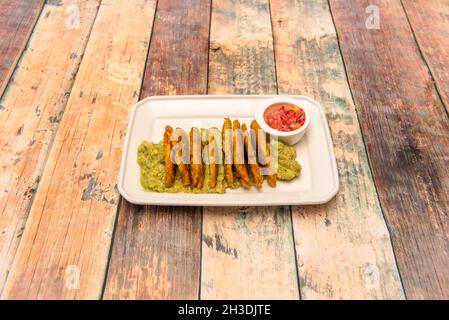 Colombian patacon with guacamole and pico de gallo in white tray on wooden table Stock Photo