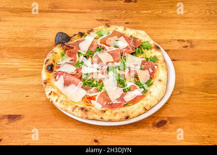 Italian Arugula Pizza with Nuts, Parmesan Cheese Slices and Prosciutto with Tomato and Mozzarella Stock Photo