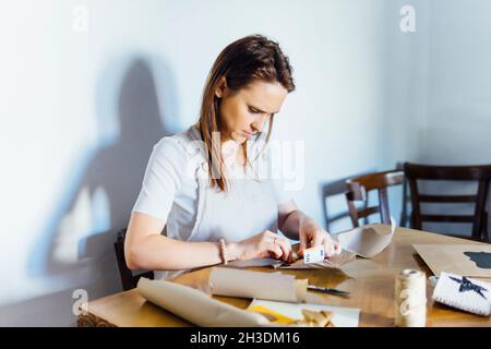 beautiful middle-aged young woman sitting at a table wrapping money. crafts concept. Christmas, wedding or birthday gift Stock Photo