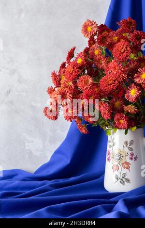 Beautiful bouquet of autumn orange chrysanthemum flowers in a vase on a blue tablecloth, part of the fall home interior Stock Photo