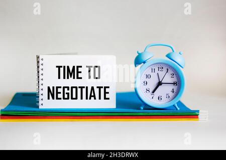 In a notebook, the text TIME TO NEGOTIATE next to multi-colored folders and a clock on a white Stock Photo