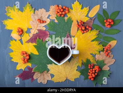 A cup of black coffee and autumn leaves on a blue wooden background. Heart shaped cup of black hot coffee. Love for coffee concept. Autumn decor, autu Stock Photo