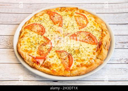 Artisan Italian pizza with thin cornmeal dough, lots of melted mozzarella cheese and slices of tomato Stock Photo