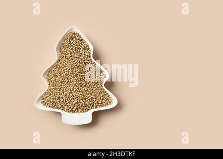 Hemp seeds in plate shape of Christmas tree isolated on beige background. View from above. Food holiday concept. Alternative creative Xmas tree. Stock Photo