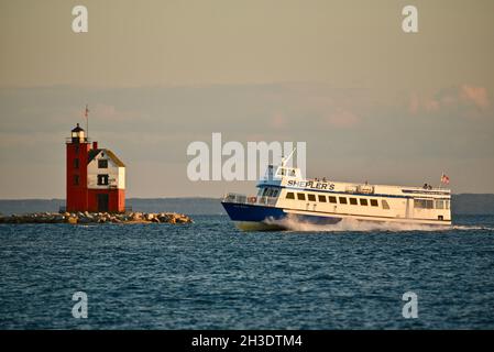 Ferry boat transporting tourists with Round Island Lighthouse across the strait from Mackinac Island in the background, Mackinac Island, Michigan, USA Stock Photo