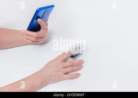The hand of an elderly woman holds a mobile phone or smartphone, measures the saturation and oxygen level in the blood with a modern medical device pu Stock Photo